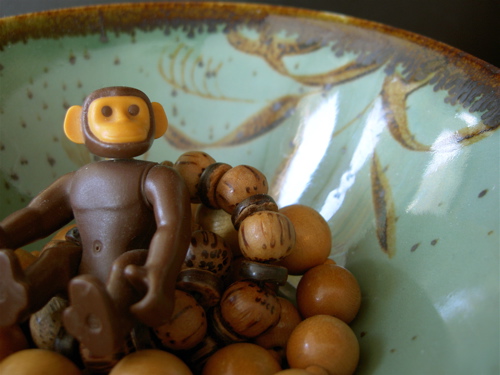 a toy monkey sitting on wooden beads in a green bowl