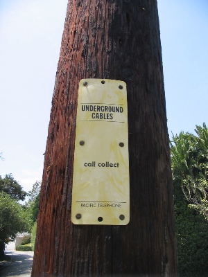 'Underground Cables. call collect. Pacific Telephone.' on the side of a telephone pole.