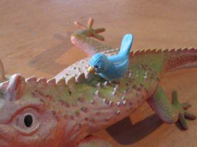 A small toy bird perched on a plastic lizard.